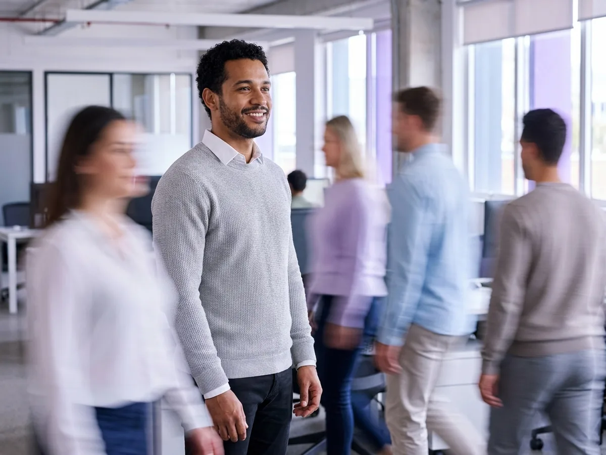 Gestor sorrindo em escritório movimentado, liderando a implantação de ERP na pequena empresa