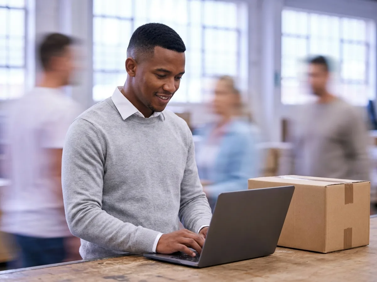 Assistente de faturamento digitando no notebook ao lado de uma caixa pronta para envio, emitindo a nota complementar de ICMS no emissor de NF-e