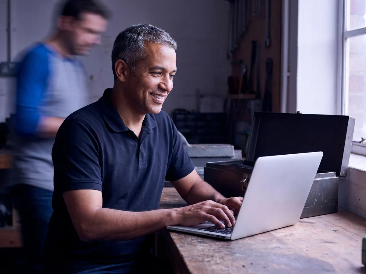 Técnico autônomo de ar-condicionado digitando no notebook na oficina para emitir a NFS-e Nacional do MEI após o serviço