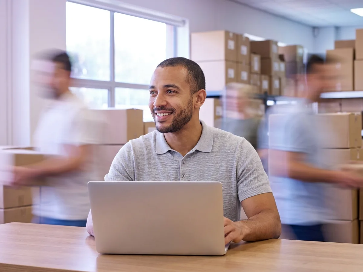 Empresário conferindo os pagamentos do dia no notebook, no estoque da empresa, com o sistema financeiro organizando contas e fluxo de caixa