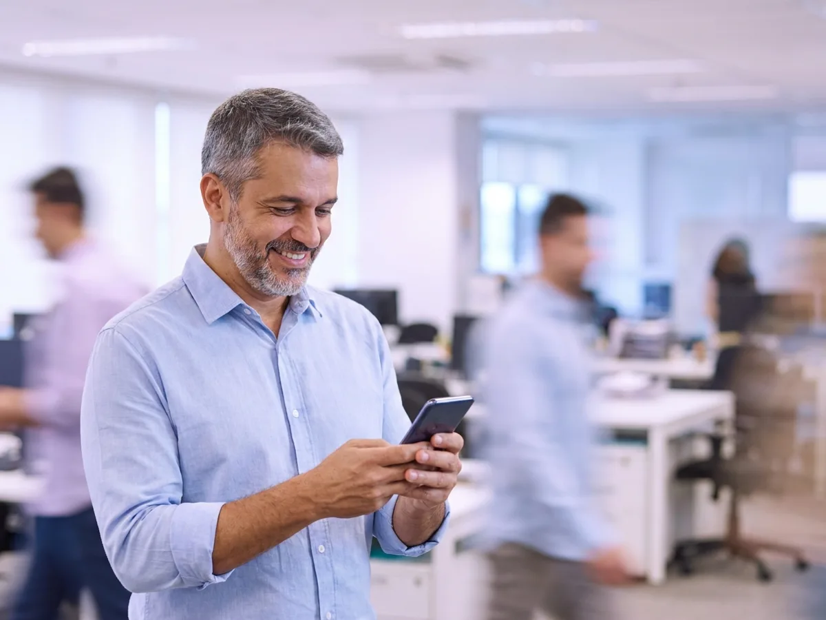 Empresário sorrindo ao ler no celular as novidades da reforma tributária e das eleições na comunidade do WhatsApp