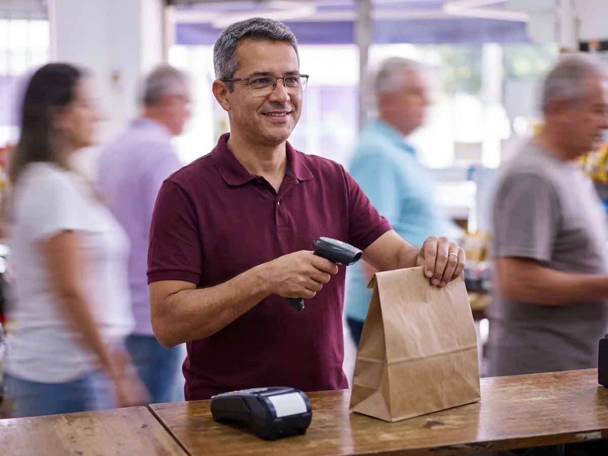 Dono de padaria passa o leitor de código de barras no caixa, mostrando o que é PDV na prática com a NFC-e emitida na venda