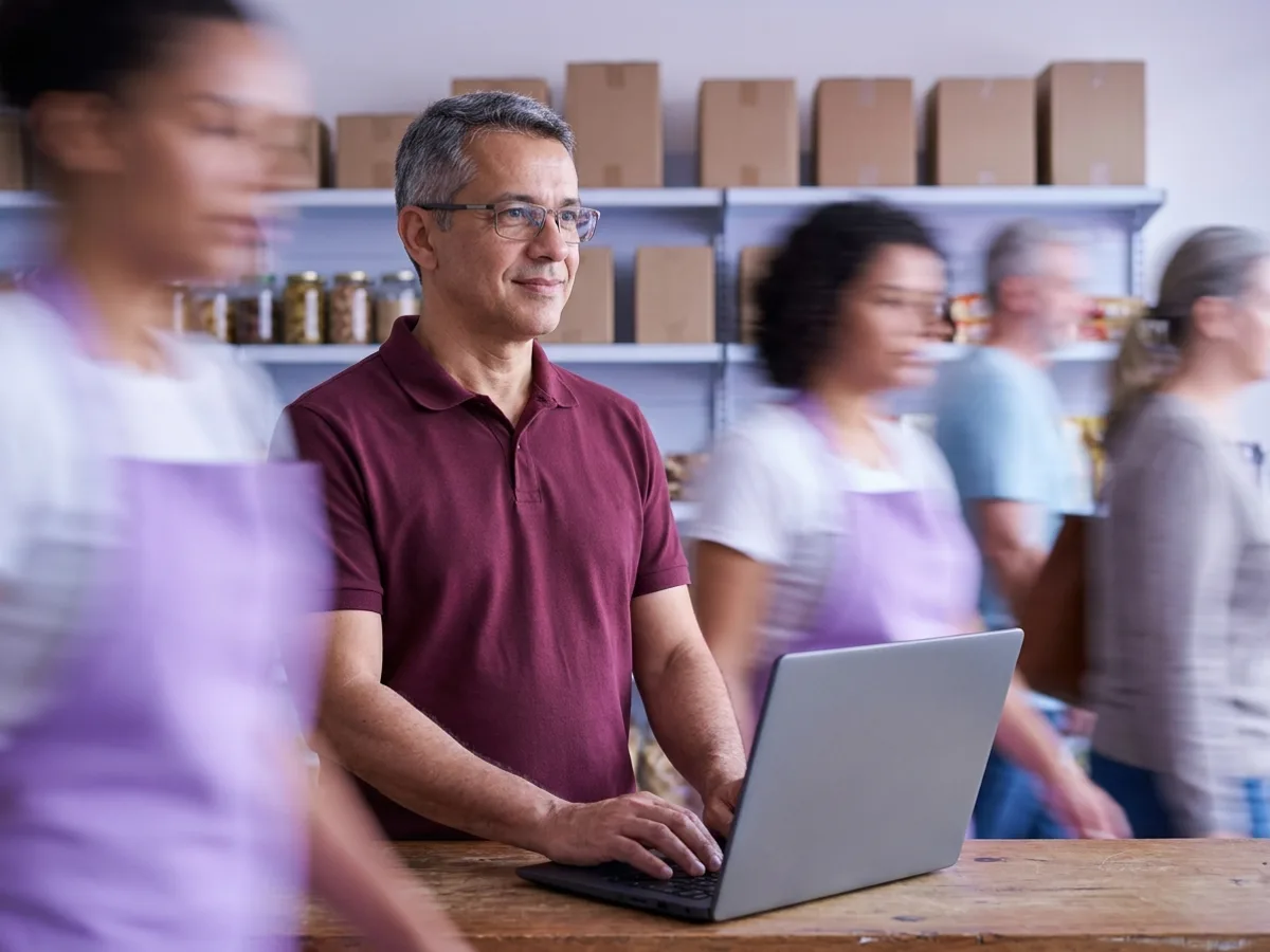 Dono de mercearia digitando no notebook no balcão para planejar a folha com o salário mínimo 2026 em um ERP para pequenas empresas
