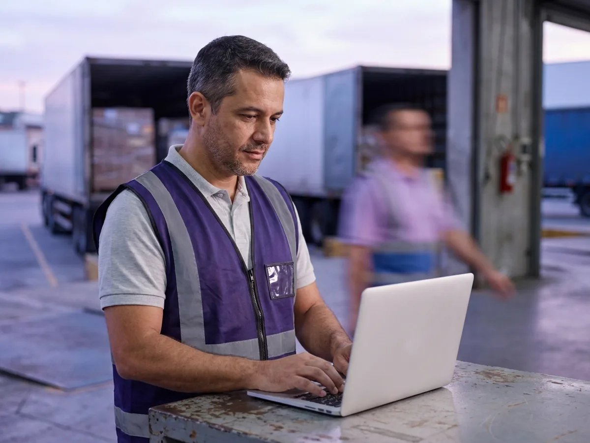 Supervisor de expedição informando o CIOT no MDF-e pelo notebook na doca, ao lado do caminhão carregado