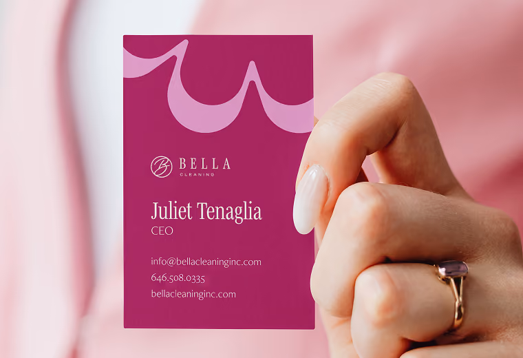 Hand holding a magenta business card with Bella Cleaning logo, showing Juliet Tenaglia as CEO with contact info including email info@bellacleaninginc.com, phone number 646.508.0335, and website bellacleaninginc.com.