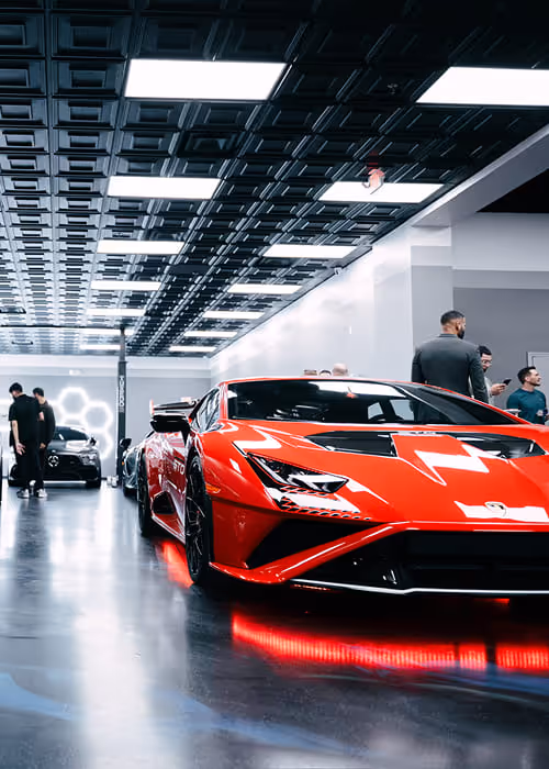 Sleek red Lamborghini sports car with illuminated red underglow lights parked indoors in a glossy showroom with a futuristic ceiling and people in the background.