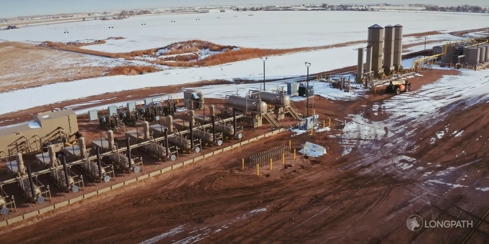 Aerial view of an industrial gas processing facility with multiple tanks, pipes, and snow-covered fields surrounding it.