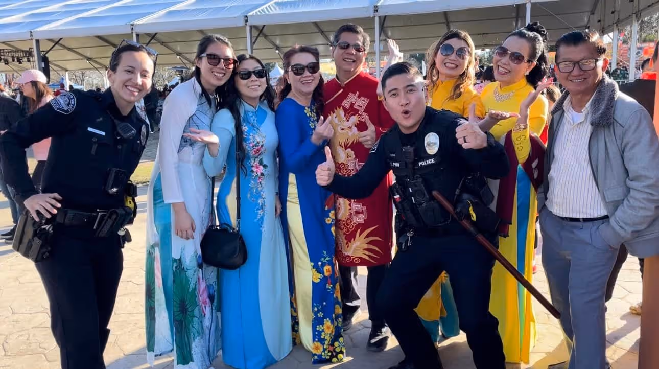 Group photo of smiling people including two police officers and several women in colorful traditional dresses at an outdoor event.