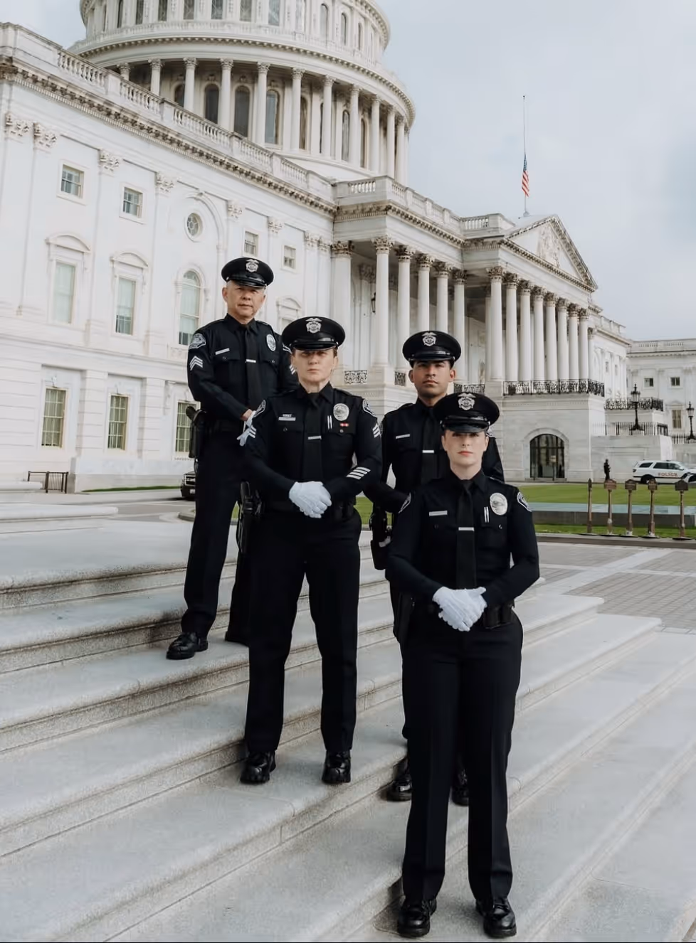 Four police officers standing on steps in front of a large white government building with columns and a dome.