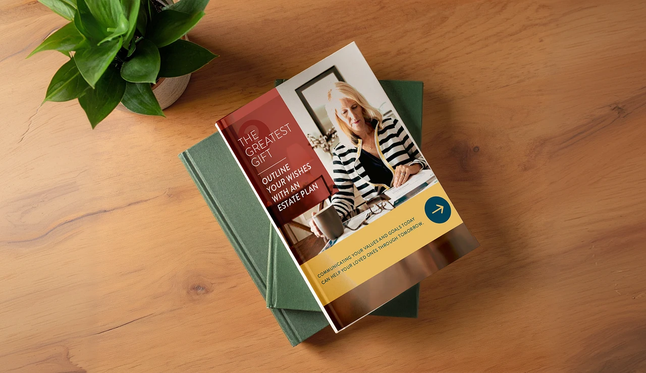 Magazine titled 'The Greatest Gift: Outline Your Wishes with an Estate Plan' resting on two green books on a wooden table, with a potted plant nearby.