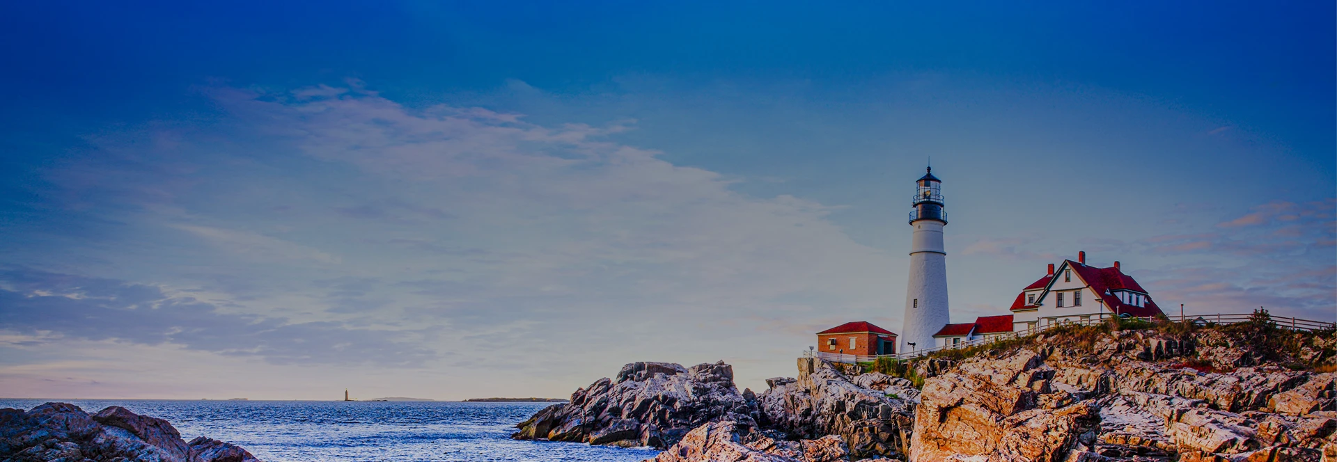 Lighthouse and buildings on rocky coastline with ocean and sky in the background.