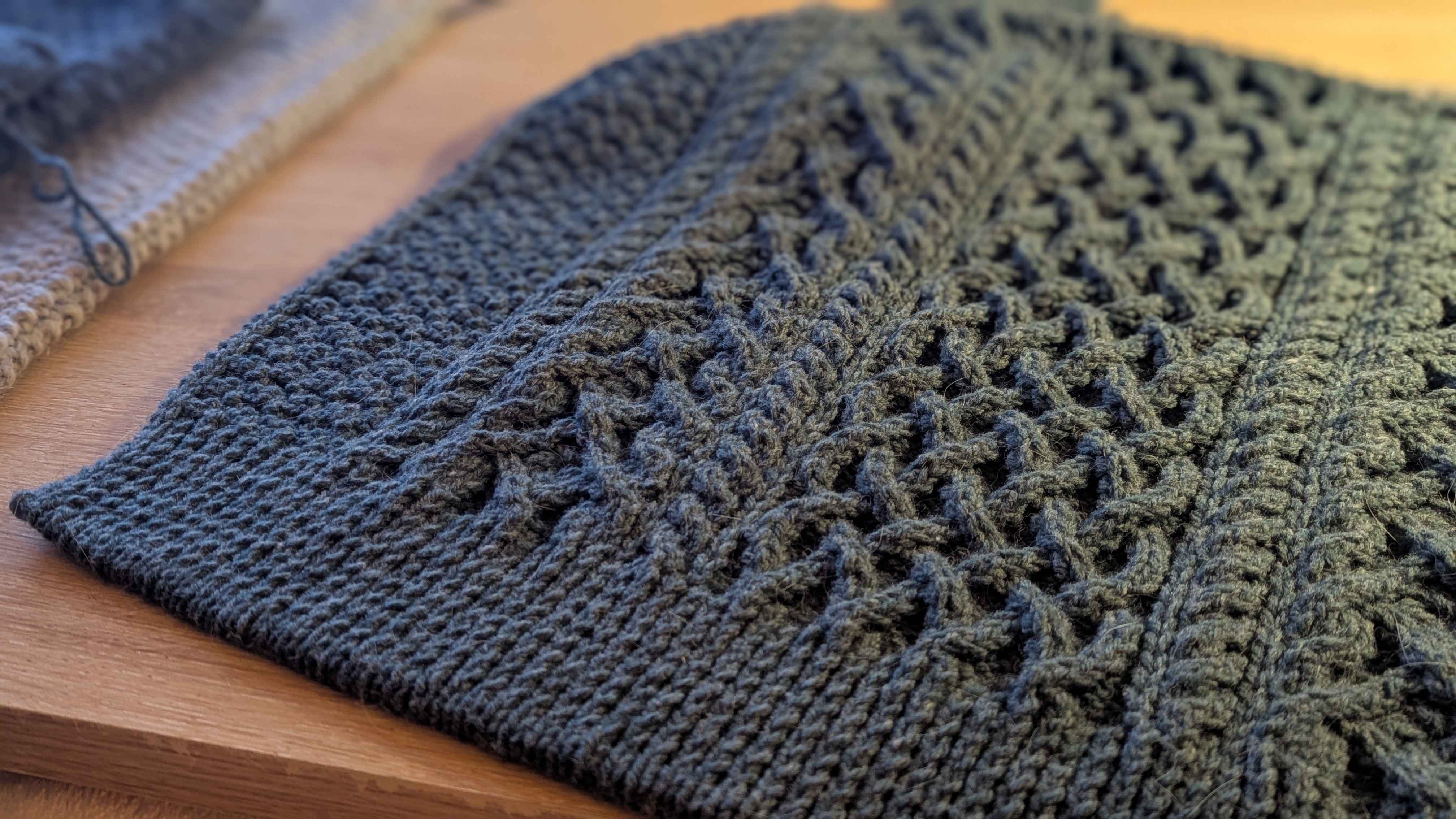 Pièce de tricot vert foncé avec torsades en cours de fabrication.