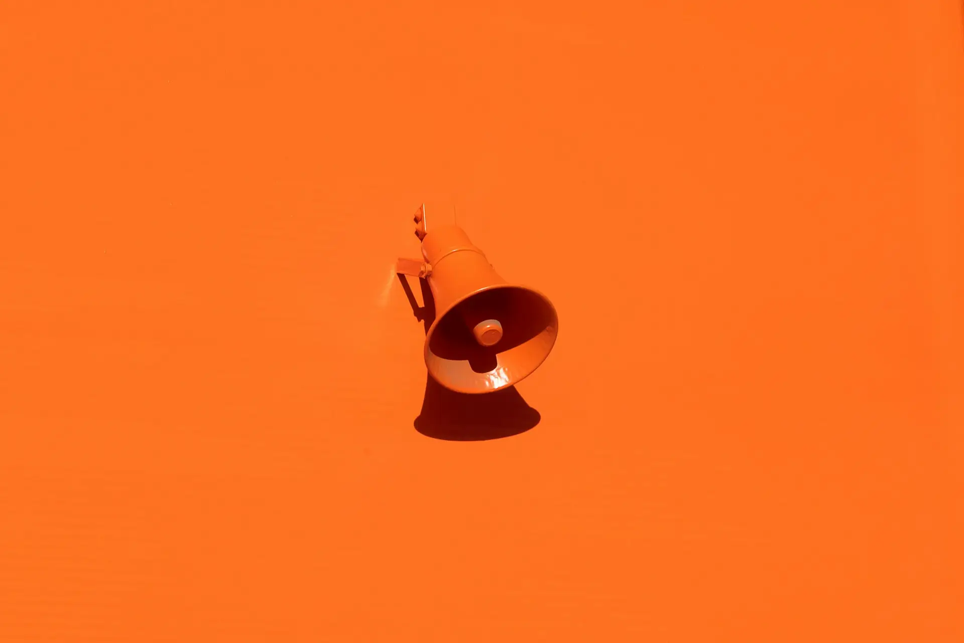 Orange megaphone mounted on an orange wall casting a shadow.