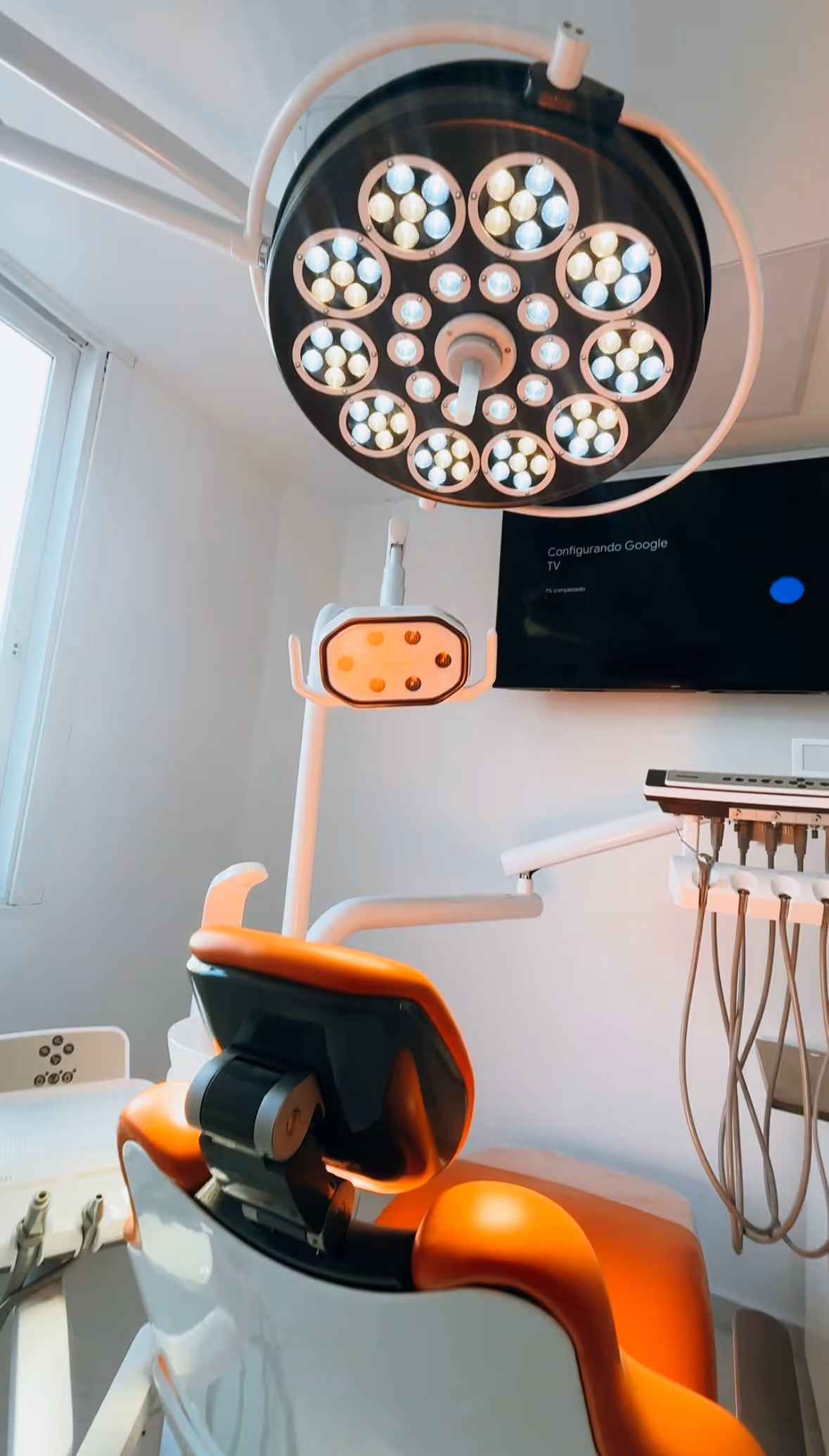 Silla y lámpara de odontología en un consultorio dental moderno con pantalla en la pared.