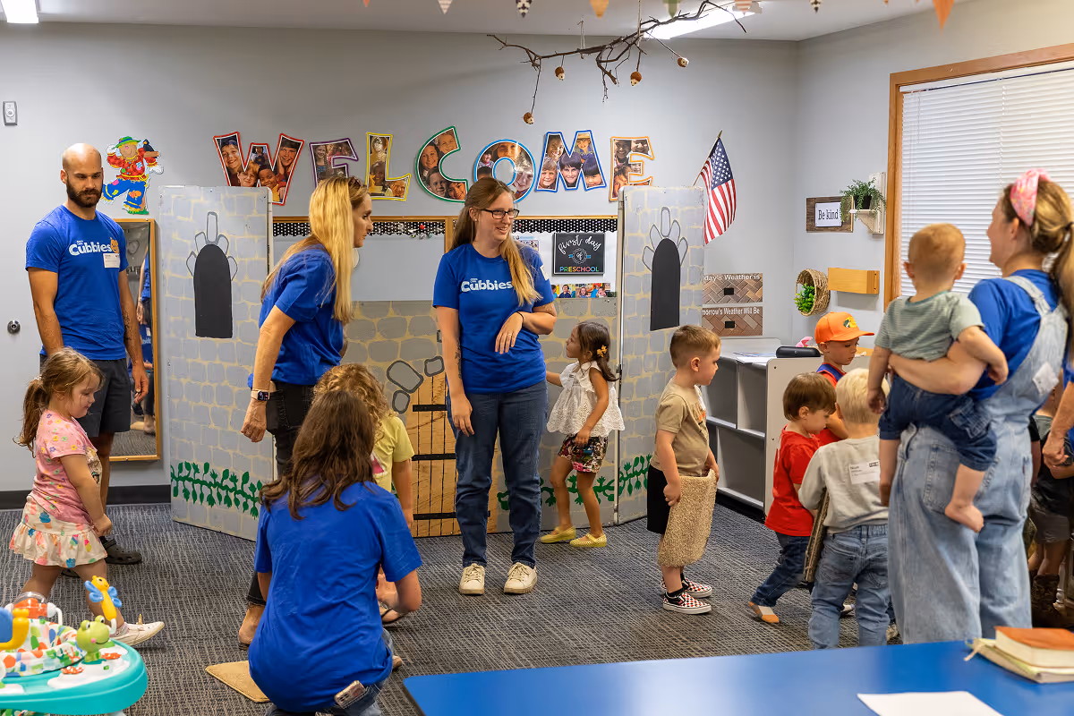 Preschool classroom with teachers in blue Cubbies shirts engaging with children playing around a cardboard castle and educational toys.