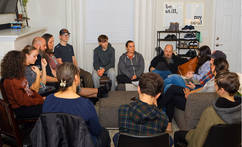 Group of people sitting in a living room in a circle, engaged in a discussion.