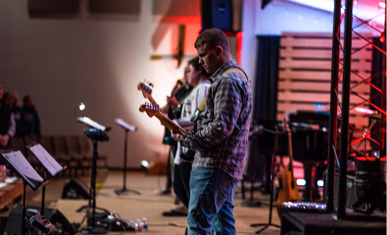 A group of musicians playing electric guitars on stage during a worship service in a church setting.