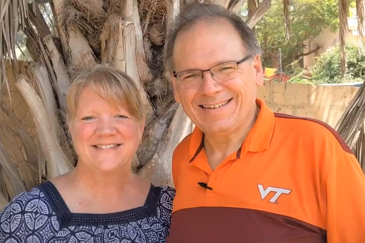 Smiling middle-aged man and woman standing outdoors in front of tree trunks.