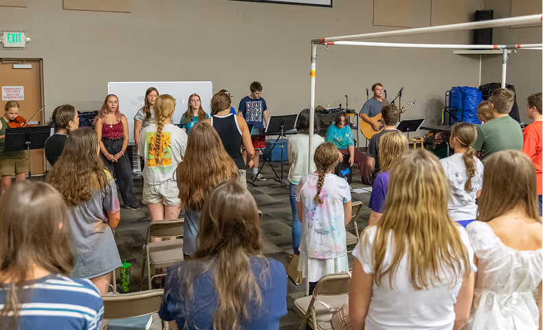 Group of young people standing and facing a small band playing music in a room with beige walls.