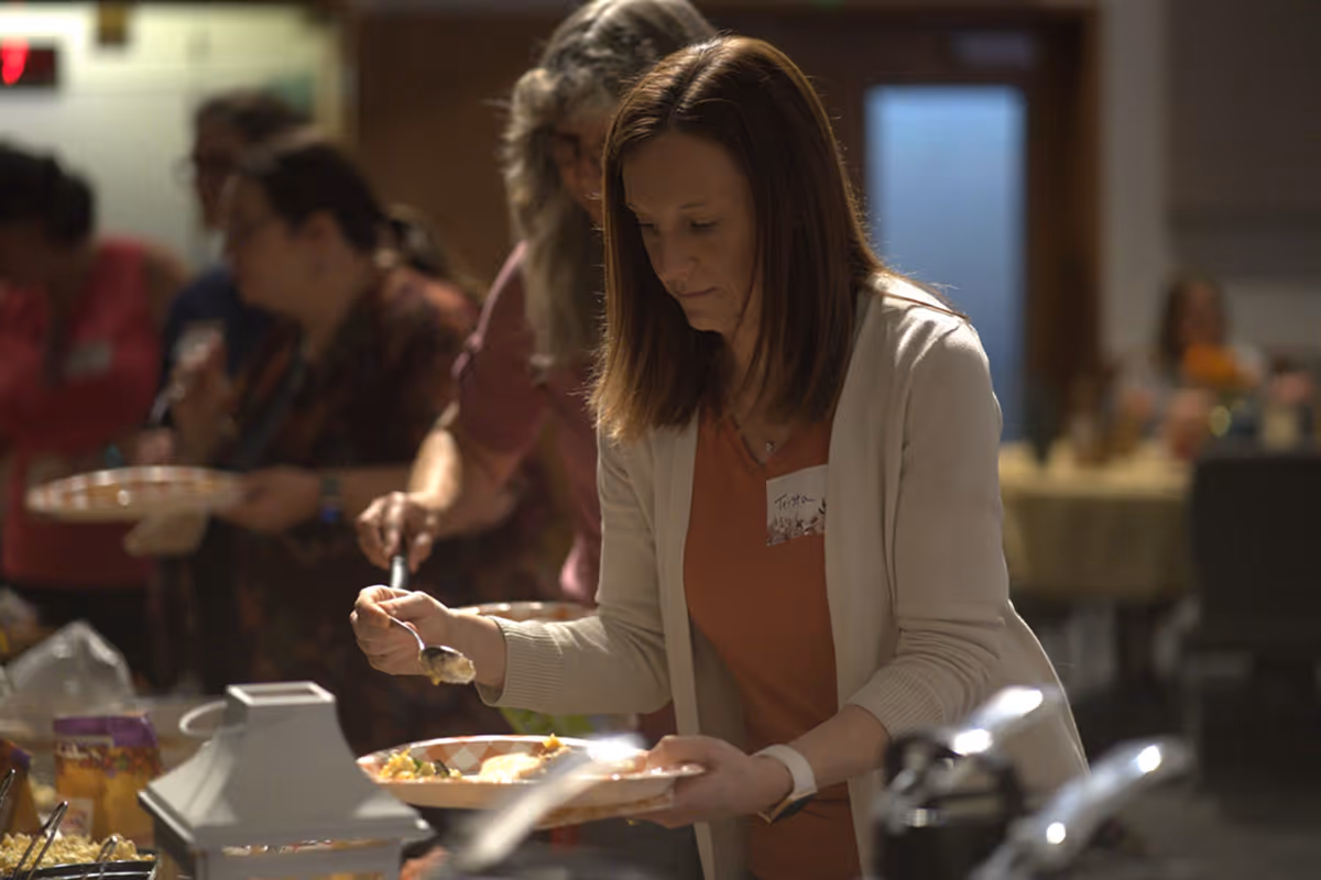 Woman serving food onto a plate at a buffet table during a social gathering.