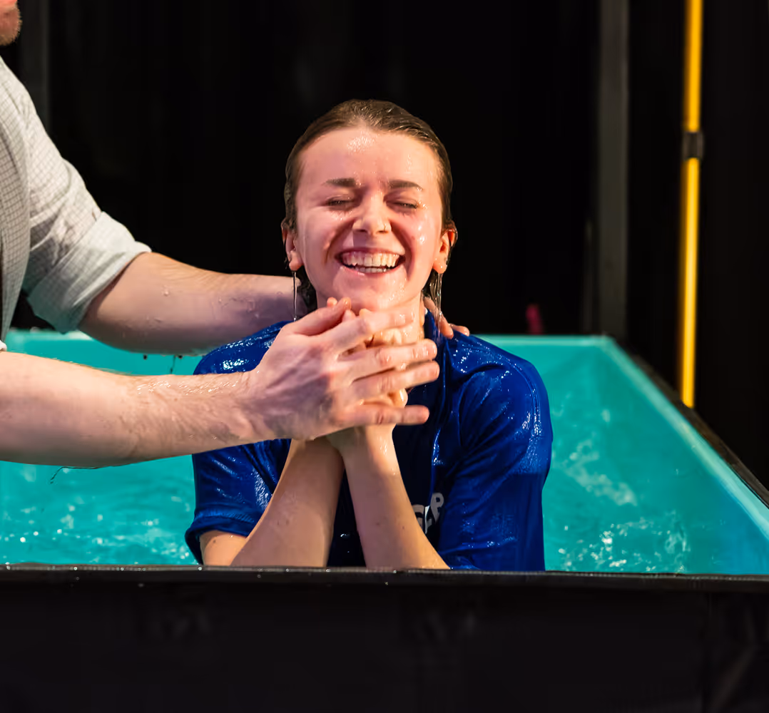 Smiling woman emerging from a baptismal pool with a person's hands supporting her neck and chin.
