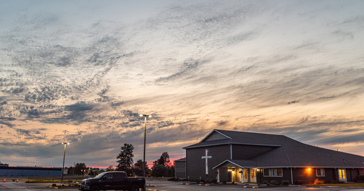 Church building with a lit cross on the side and sunset sky with scattered clouds.
