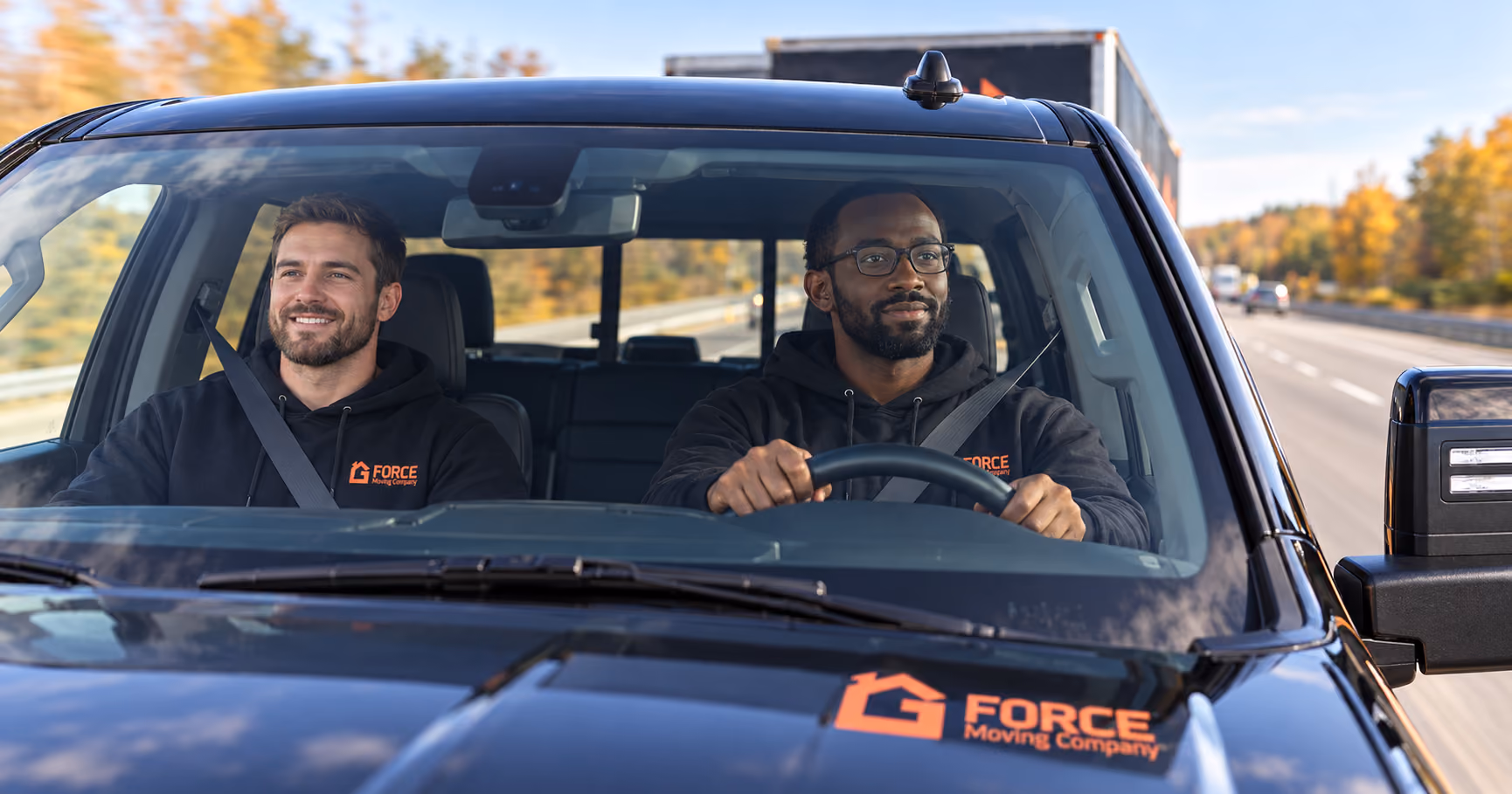 Close view through the windshield of two G Force movers travelling in their branded truck along a highway.