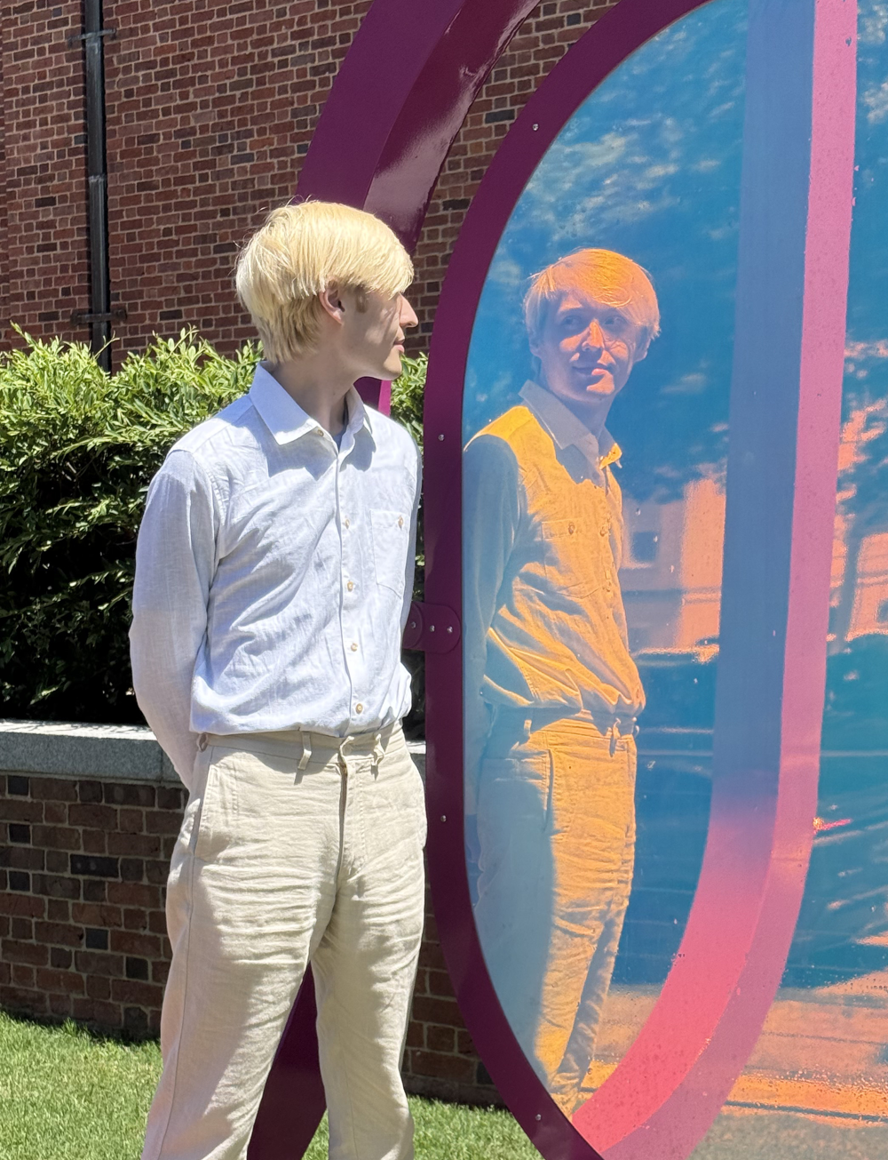 A picture of Trey Anderson's dressed in white formal attire looking at a reflection of himself in a colorful mirror.