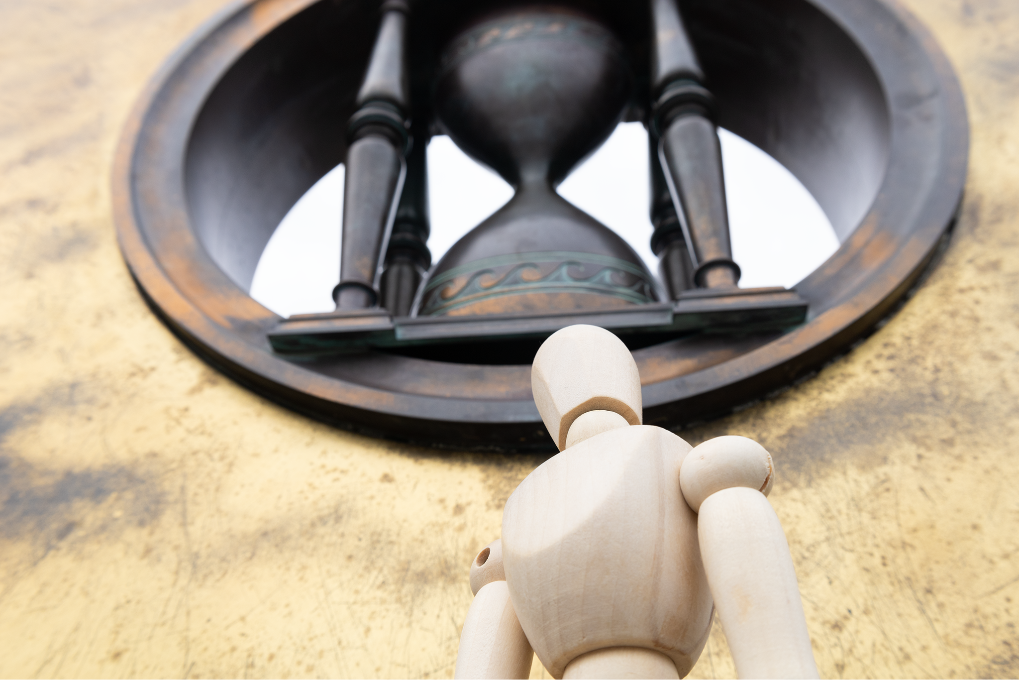 A photograph featuring a drawing mannequin outside looking up to a hourglass sculpture