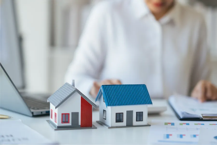A real estate professional working at a desk with miniature house models, representing home buying, property investment, and mortgage planning.
