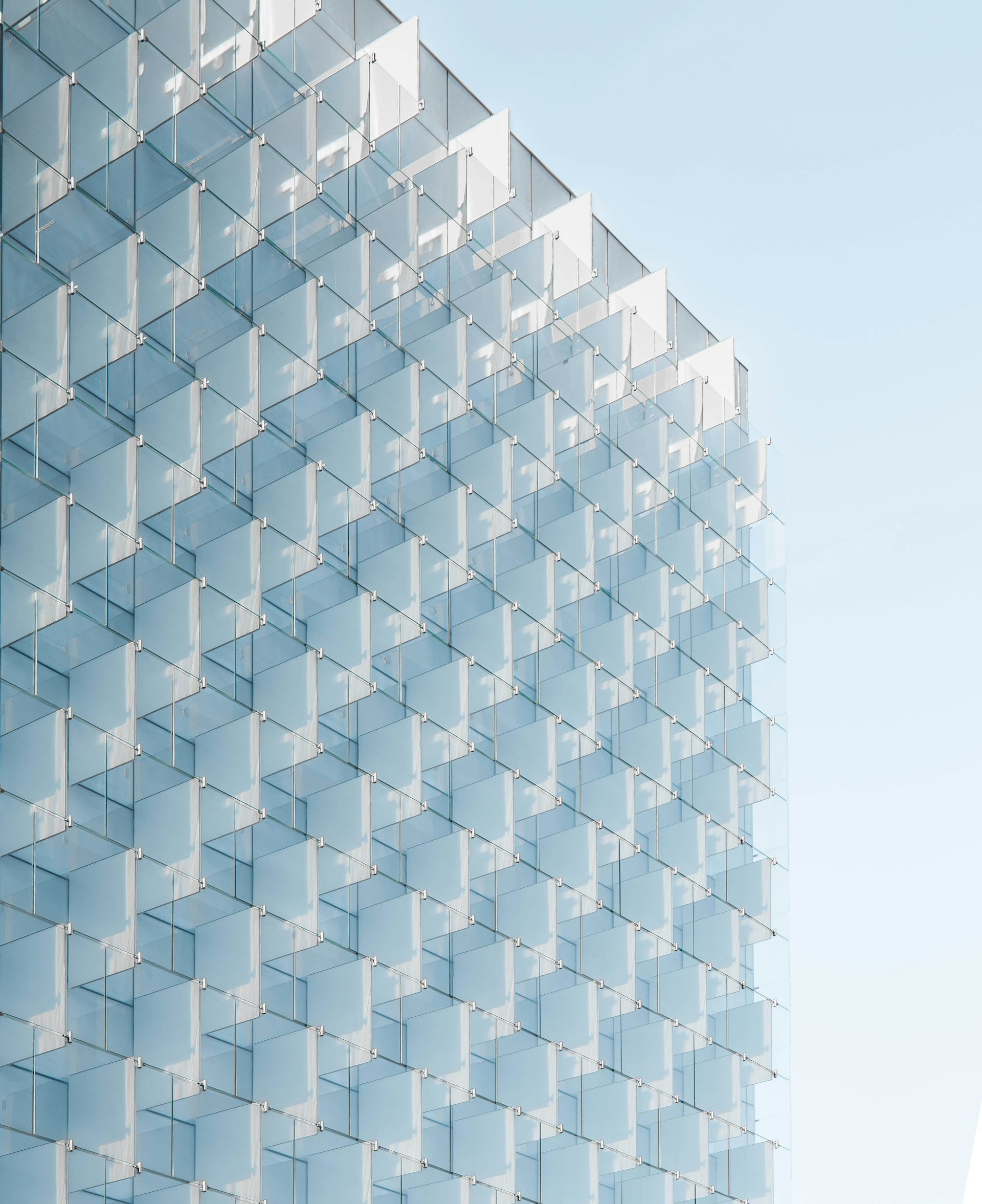 Façade d'un bâtiment moderne avec des panneaux de verre carrés en relief reflétant le ciel.