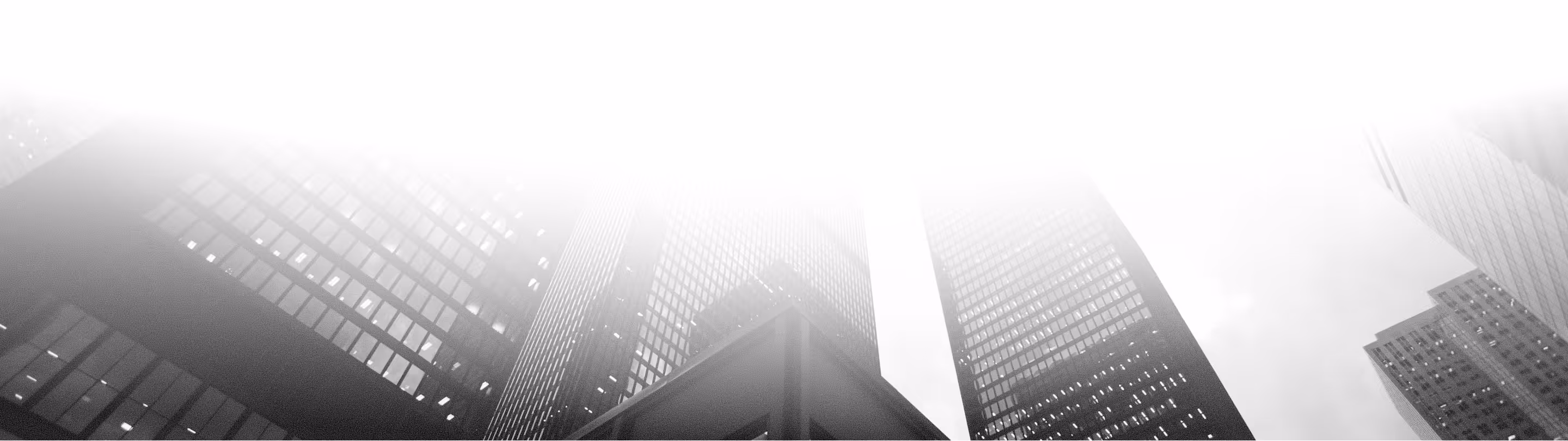 Low-angle view of tall skyscrapers with reflective glass windows fading into white sky.