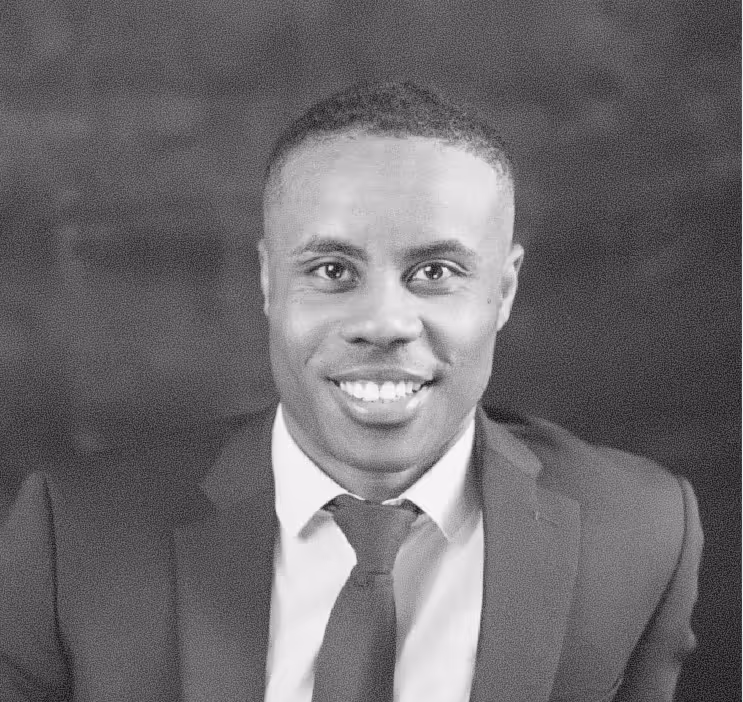 Smiling man in a dark suit and tie against a plain dark background.