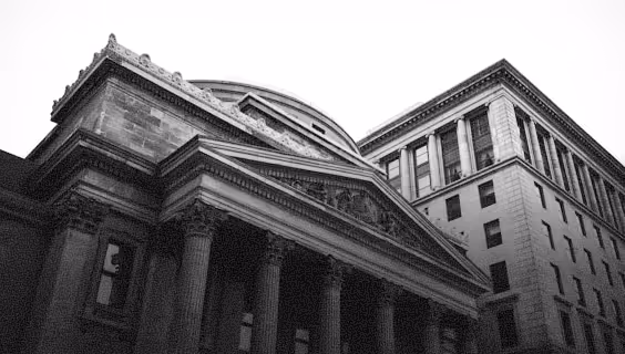 Black and white photo of classical architecture with large columns and an adjacent tall modern building.