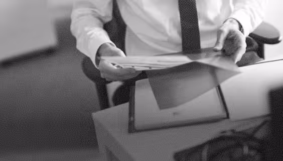 Person in white shirt and black tie holding documents over a desk with a tablet and keyboard.