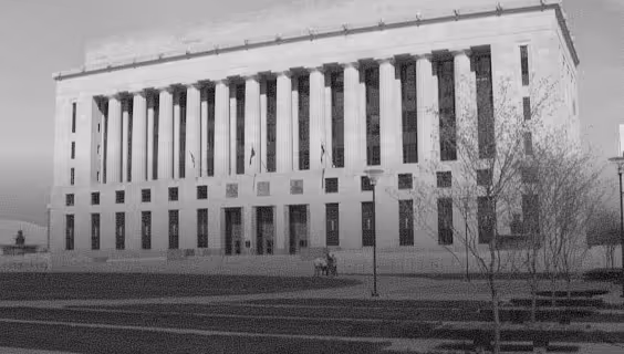 Large neoclassical building with tall columns and flagpoles in front, surrounded by a grassy area and leafless trees.
