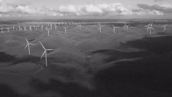 Aerial view of numerous wind turbines spread across a vast green landscape under a cloudy sky.