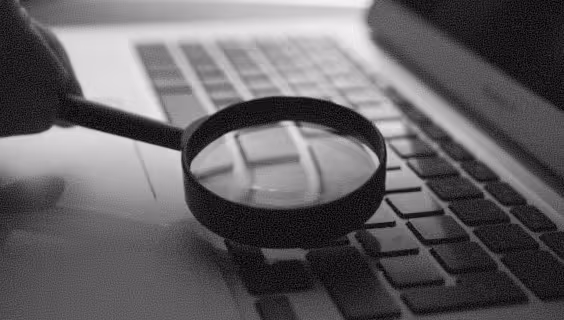 Magnifying glass positioned over a laptop keyboard in grayscale.
