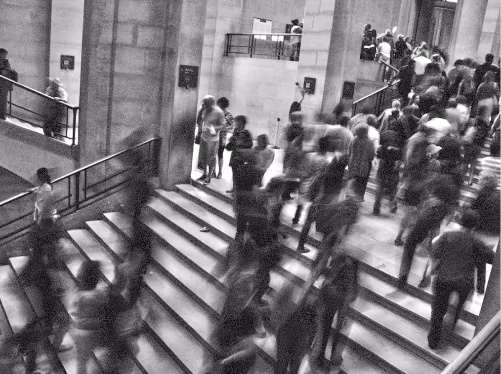 Black-and-white photo of a busy indoor staircase with blurred people walking up and down.