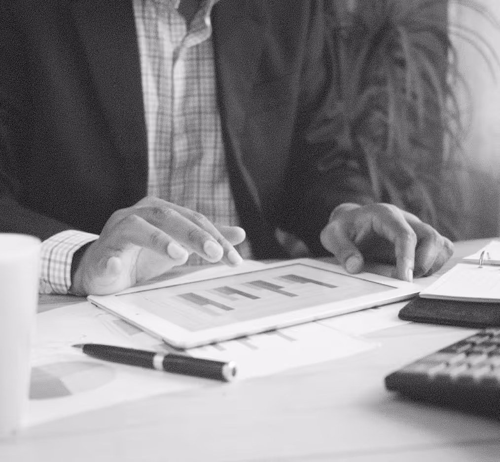 Person in business attire interacting with a tablet displaying bar charts on a cluttered desk.