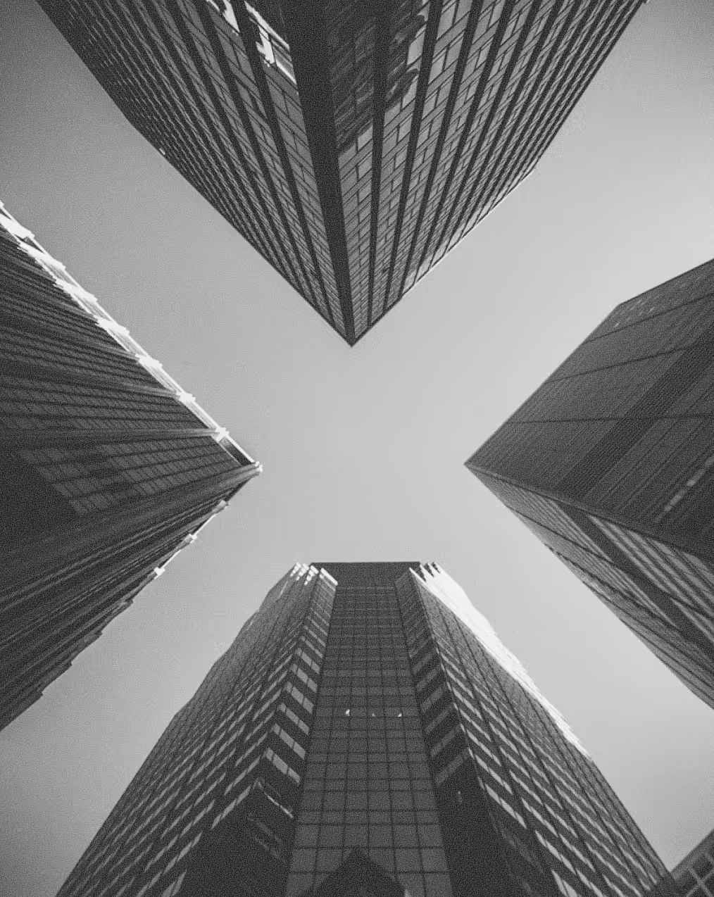 Black and white low-angle view of four skyscrapers converging toward the sky.