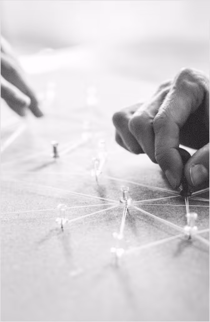 Close-up of hands connecting transparent pins on a surface with interwoven strings, symbolizing network or connection.