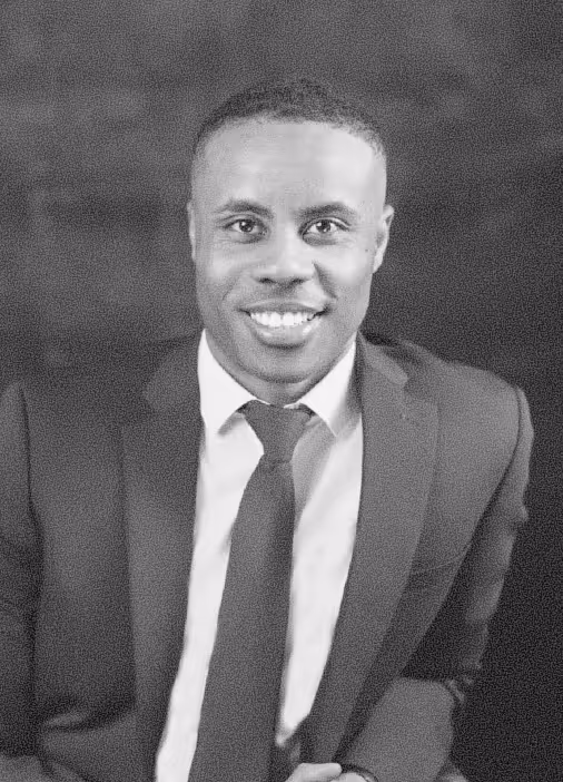 Smiling man in a dark suit and tie against a dark background.