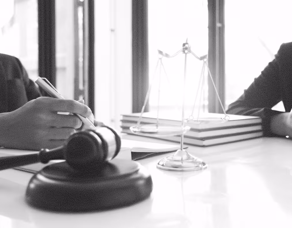 Close-up of a gavel, scales of justice, and a person writing on paper with books in the background.