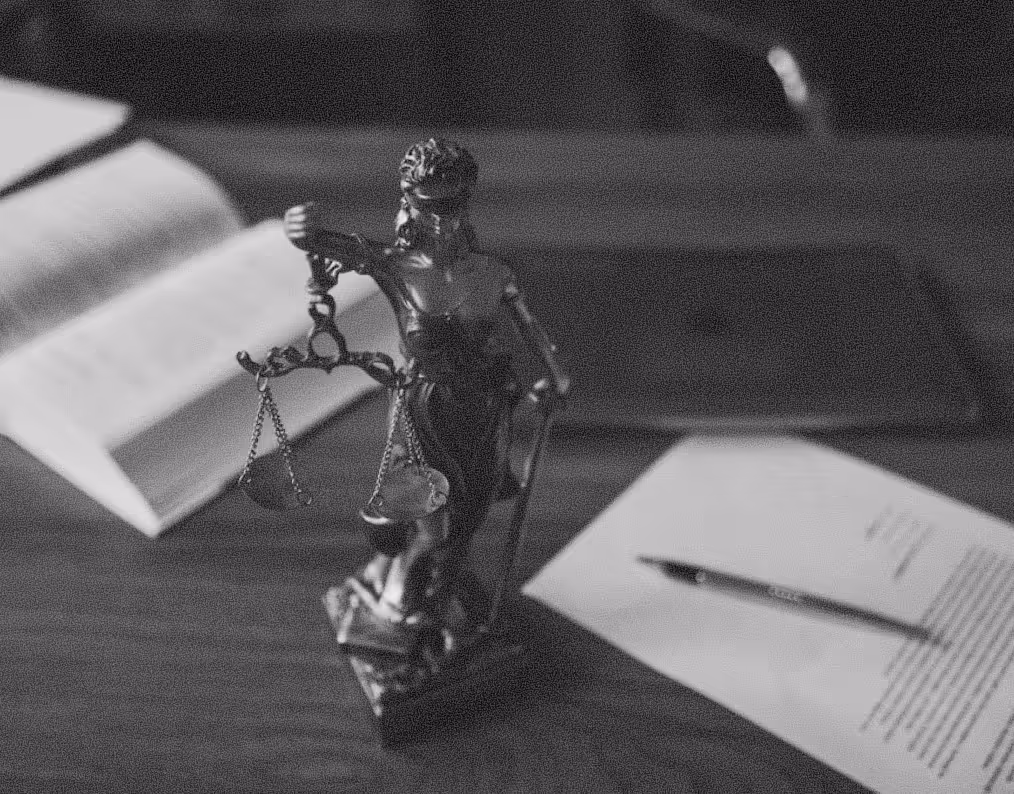 Bronze statue of Lady Justice holding scales, placed on a wooden desk with an open book and a document with a pen.