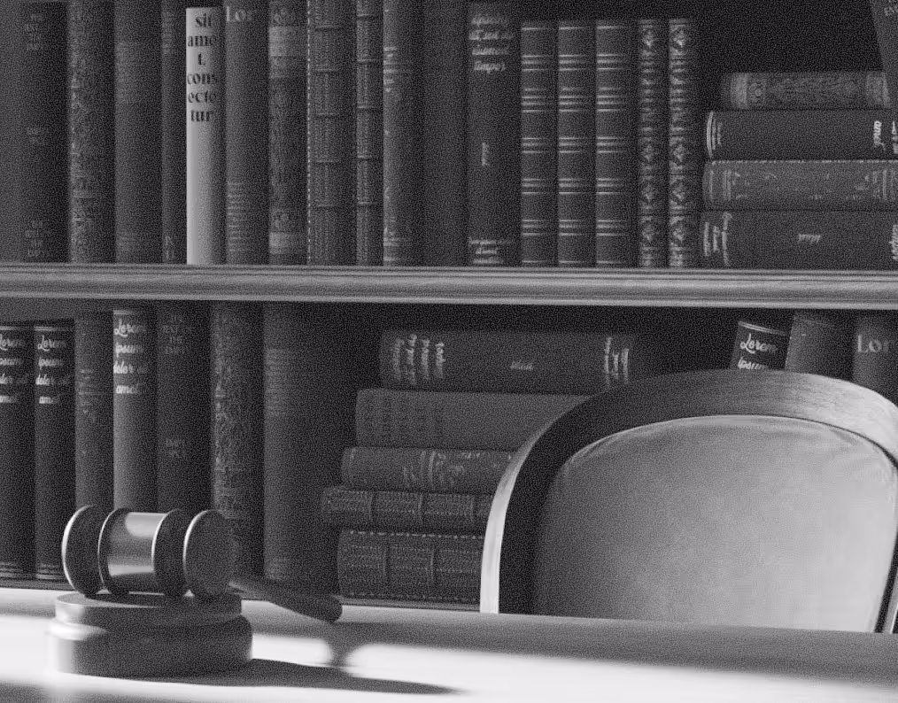 Wooden judge's gavel on a desk with a bookshelf and an empty chair in the background.