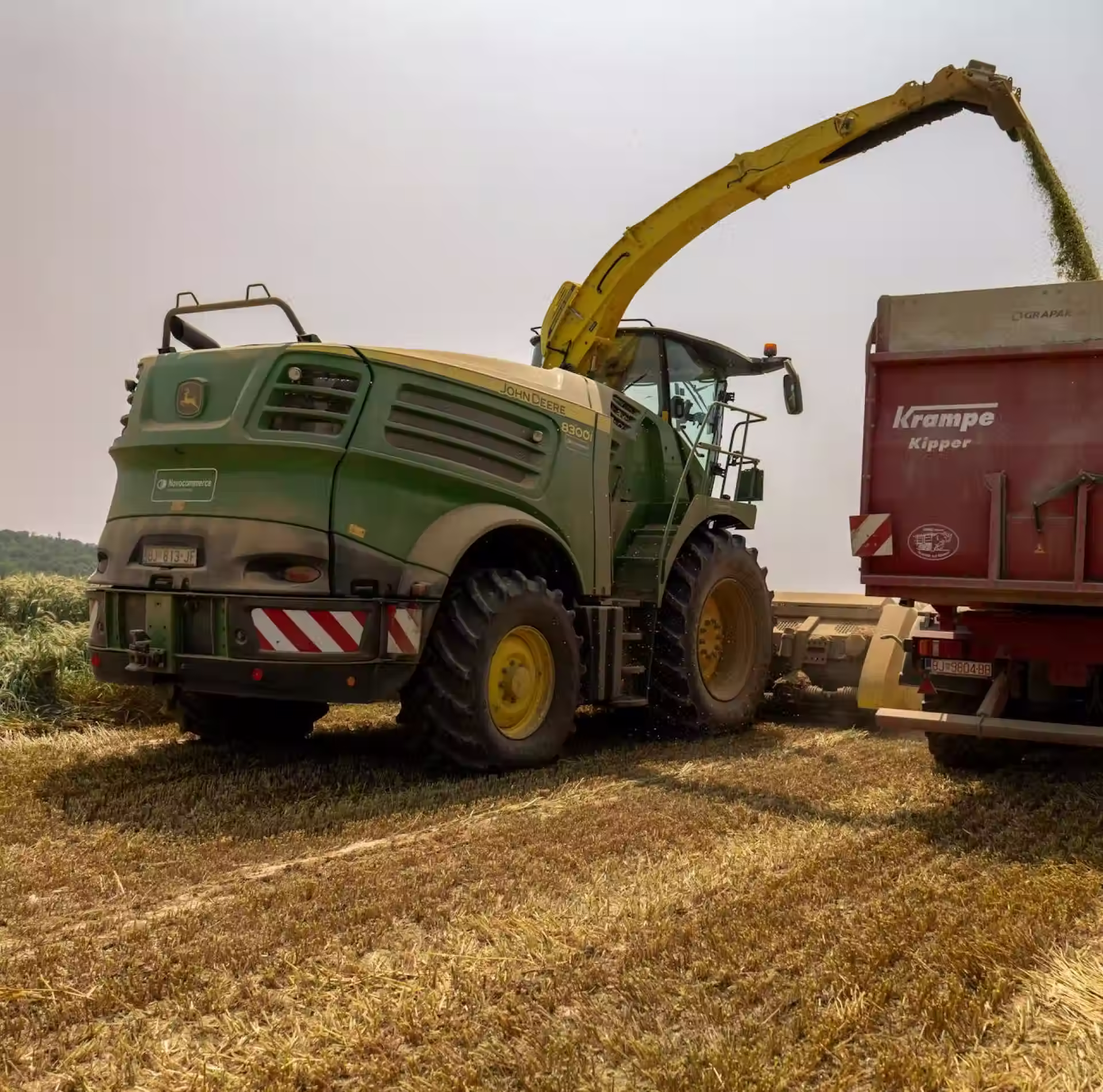 John Deere forage harvester unloading chopped crop into a Krampe Kipper trailer in a field.