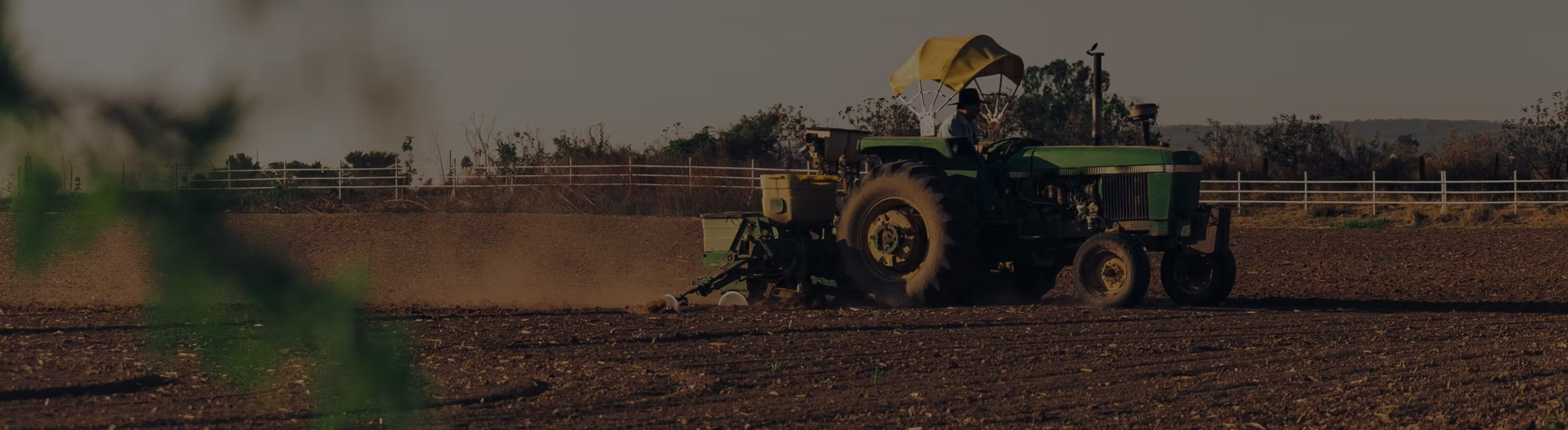 A tractor with a canopy plowing a field at sunset with a person driving it.