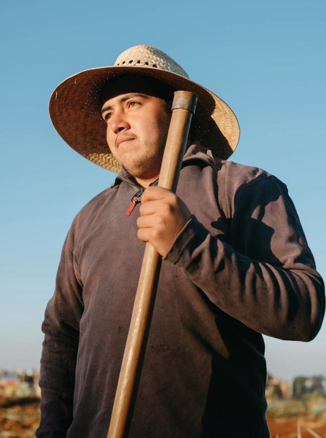 Man wearing straw hat and dark shirt holding a wooden tool handle against a clear sky.