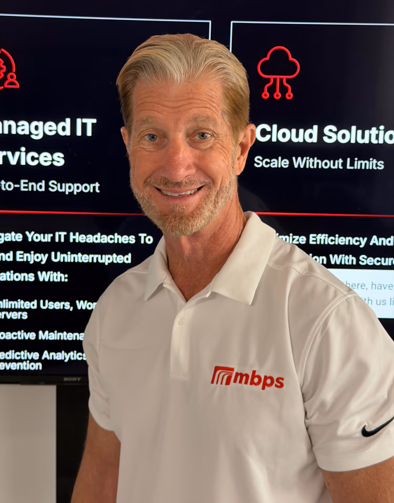 MBPS managed IT services representative smiling in front of cloud solutions and managed IT services display screens